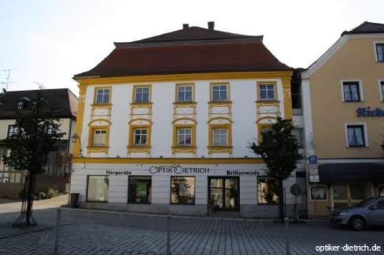 Fassade eines Optikergeschäfts mit gelbem Stuck, Schaufenstern und barocker Architektur.